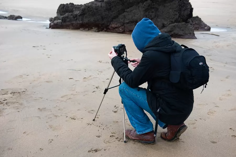 person on a beach with a tripod and camera photographing a landscape scene